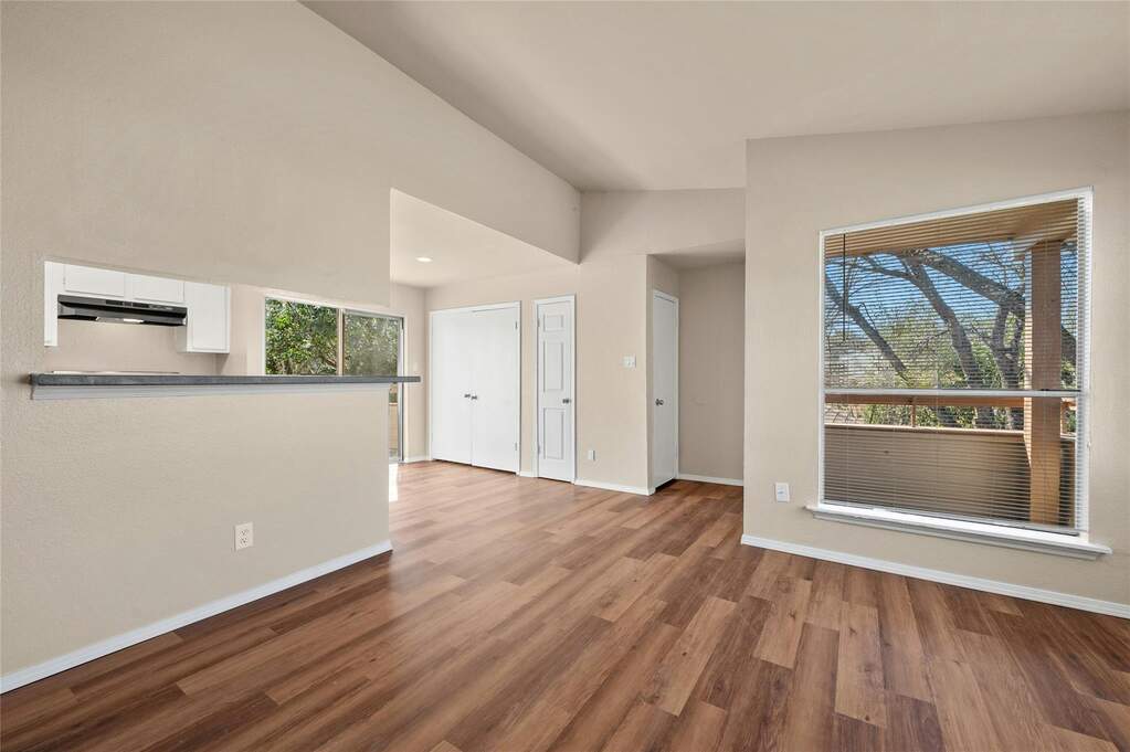 Spacious living area featuring wood-finish flooring, vaulted ceilings, and a pass-through window to the kitchen