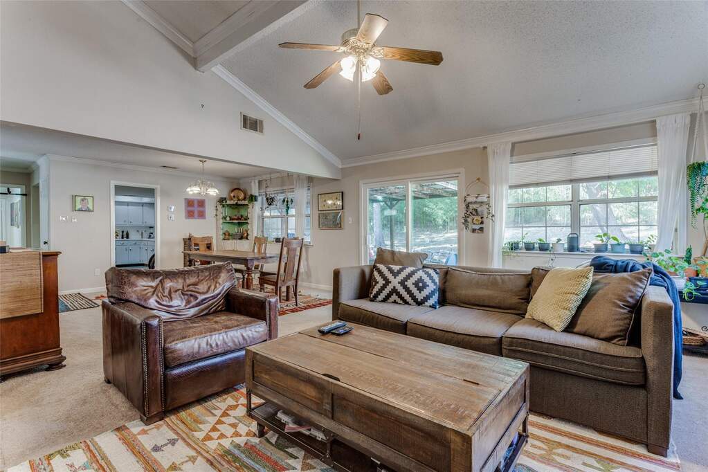 Living area featuring light colored carpet, ornamental molding, high vaulted ceiling, beam ceiling, and ceiling fan