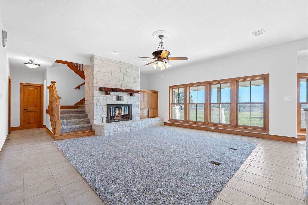 Unfurnished living room featuring stairway, ceiling fan, light tile patterned floors, and a fireplace