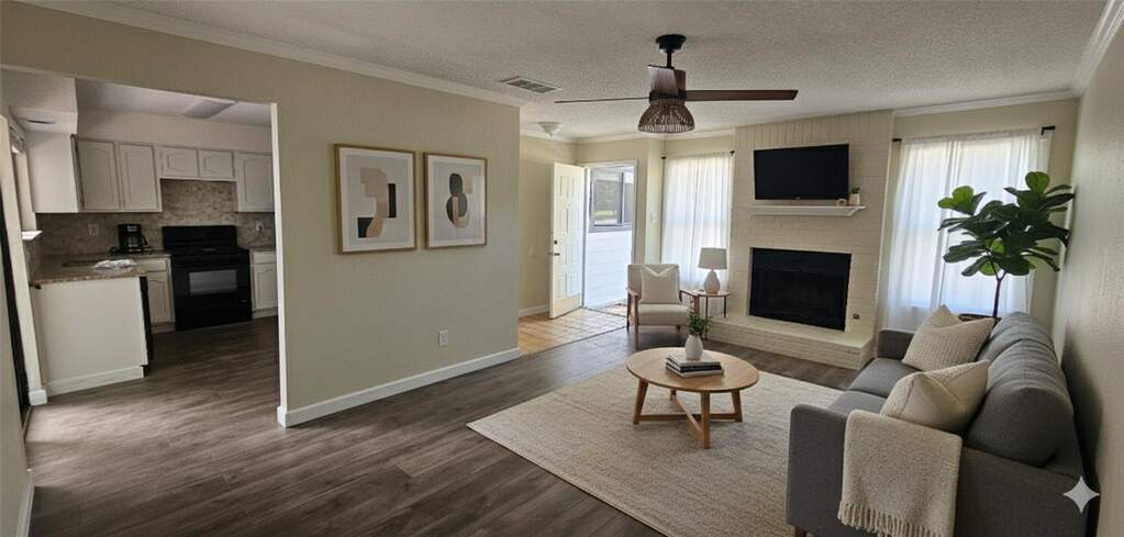 Living area featuring a fireplace, a textured ceiling, ceiling fan, crown molding, and dark wood-style flooring