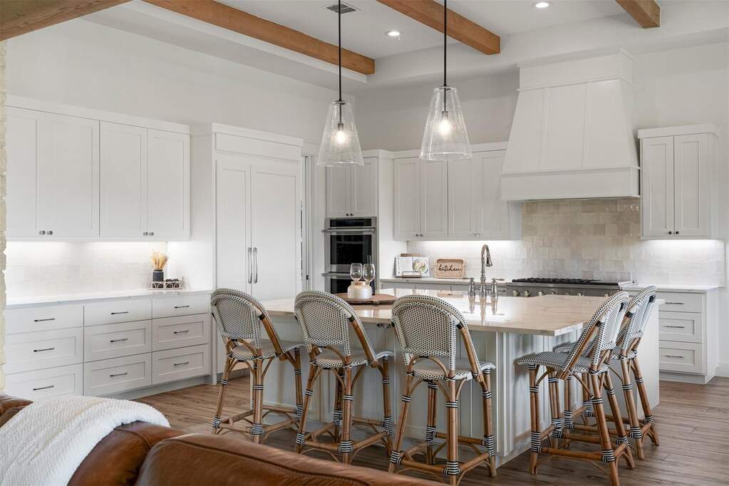 Warm wood-beamed ceilings complement the white shaker cabinetry, creating a space that feels both high-end and welcoming