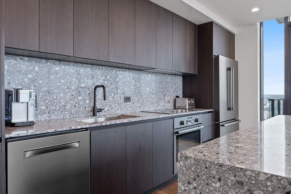 Representative Photo. Kitchen featuring custom Italkraft cabninetry, terrazzo backsplash, waterfall-edge terrazzo countertops, black stainless steel Bosch appliances, and pendant lighting abo