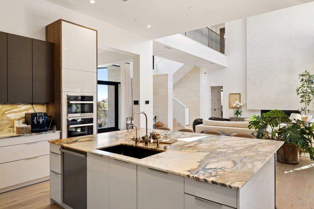 Two tone kitchen with light wood-type flooring, modern cabinets, light stone countertops, open floor plan, and a high ceiling